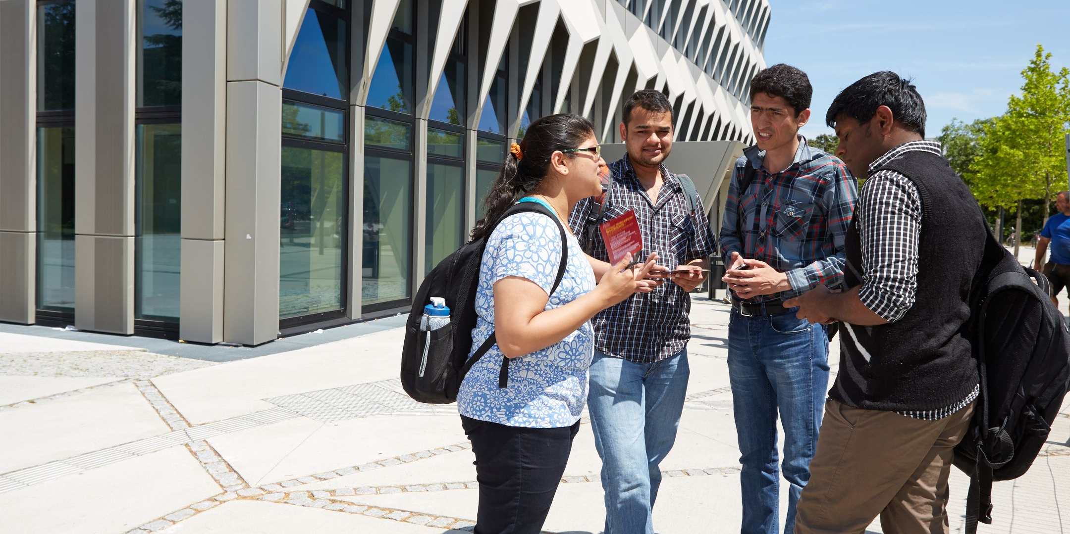 Internationale Studierende stehen auf dem Campus vor dem Hochhaus der h-da und reden fröhlich miteinander